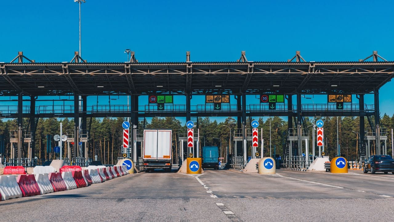 Cars passing through toll booths on a busy highway under a clear sky