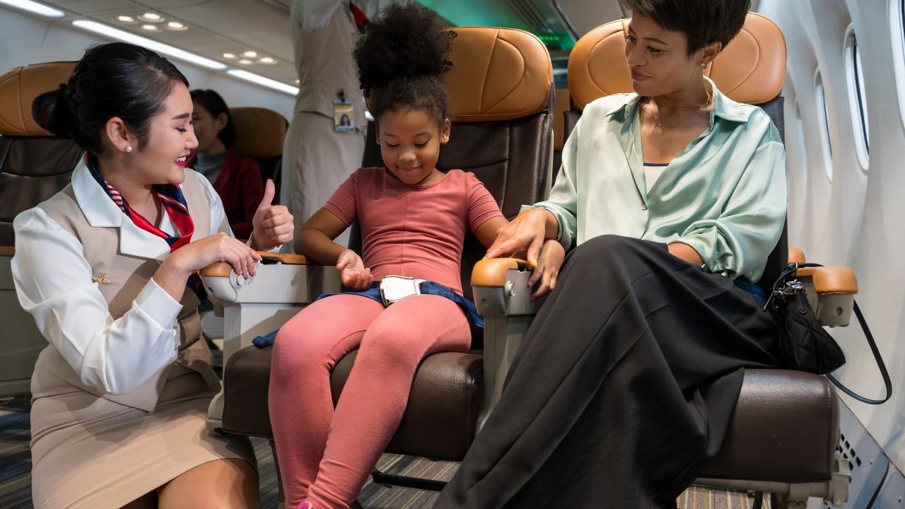 Flight attendant speaking with a young child seated beside her mother on an airplane