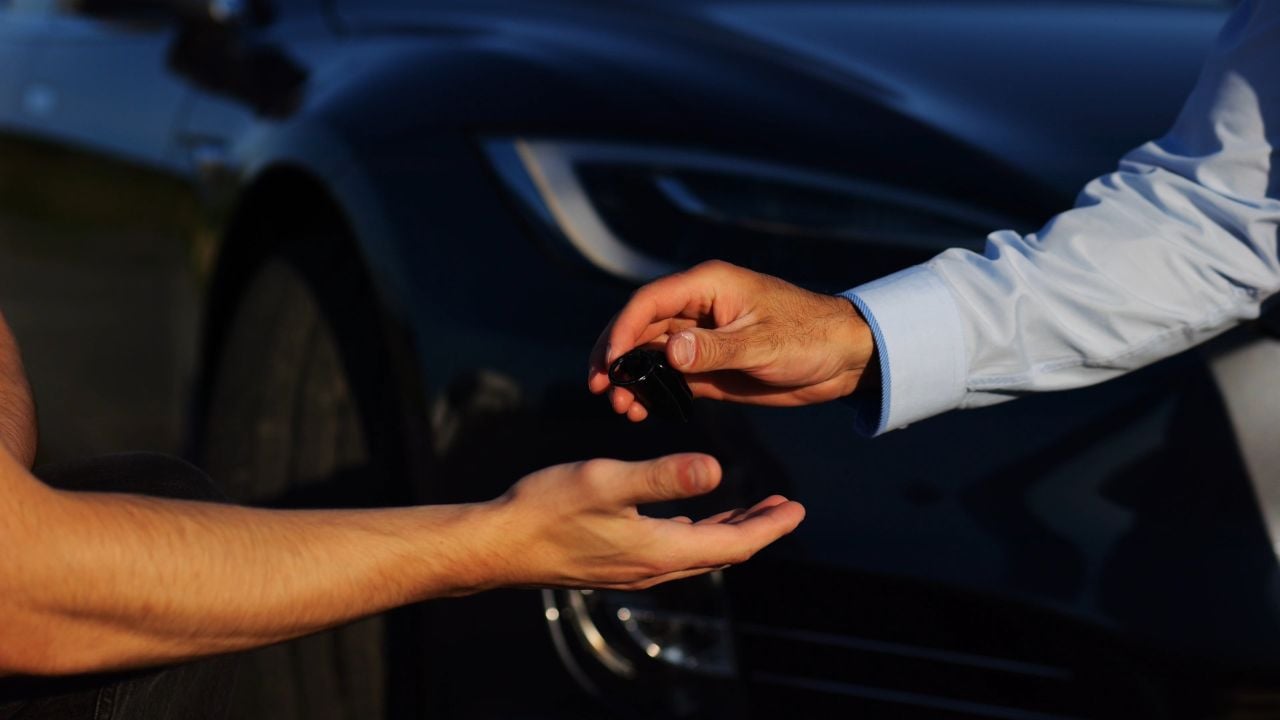 Car key being handed to a driver after a rental or purchase agreement