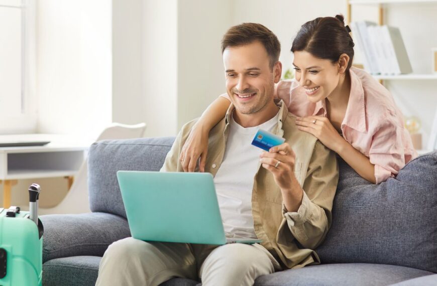 Couple with laptop makes online credit card payment at home. they plan travel, compare deals, and manage costs beside a suitcase. Concept secure payment, holiday trip, vacation and travel booking.