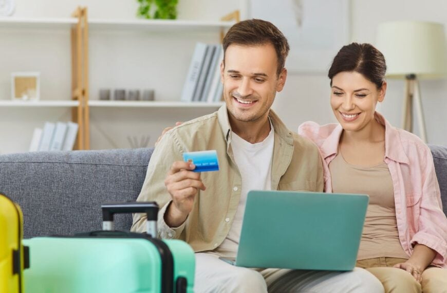 Couple with laptop makes online credit card payment at home. they plan travel, compare deals, and manage costs beside a suitcase. Concept secure payment, holiday trip, vacation and travel booking.