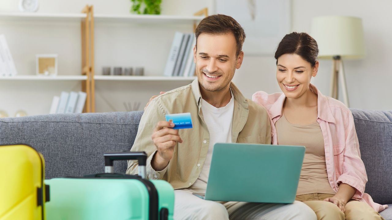 Couple with laptop makes online credit card payment at home. they plan travel, compare deals, and manage costs beside a suitcase. Concept secure payment, holiday trip, vacation and travel booking.