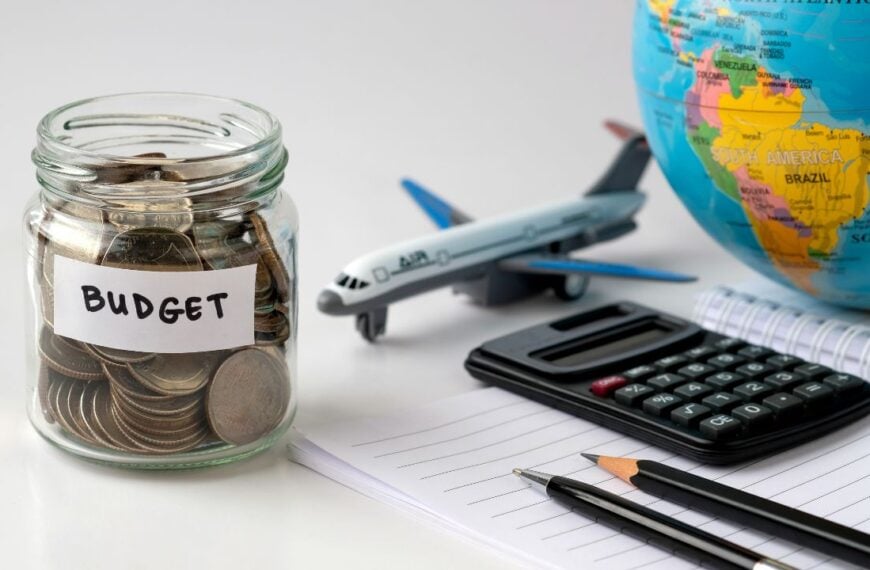Budget jar with coins, calculator, globe and airplane model symbolizing travel savings, financial planning, holiday budget and international trip preparation for future vacations worldwide.