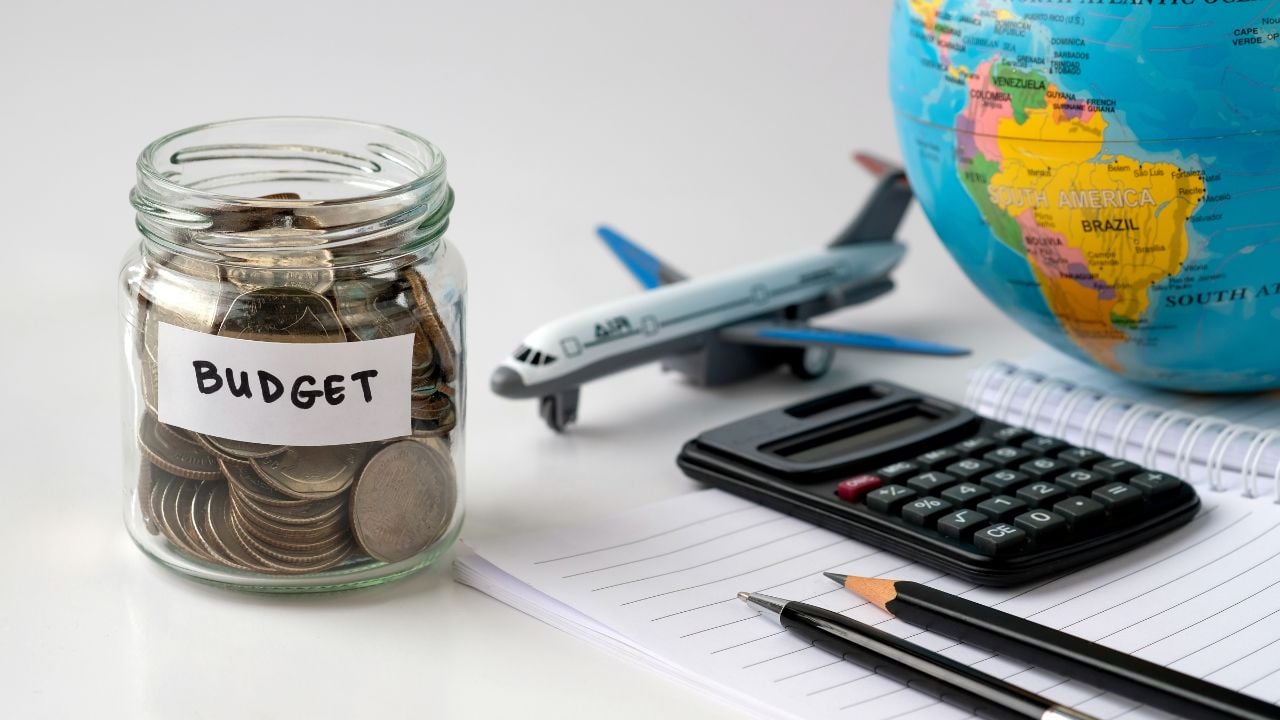 Budget jar with coins, calculator, globe and airplane model symbolizing travel savings, financial planning, holiday budget and international trip preparation for future vacations worldwide.
