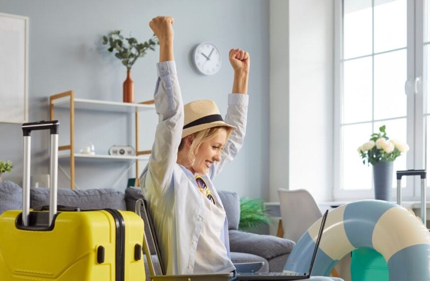Joyful woman tourist happy to reserve travel ticket, going to spend summer vacations abroad, packed things in suitcase, focused at laptop screen and clenching fists with success. Tourism concept