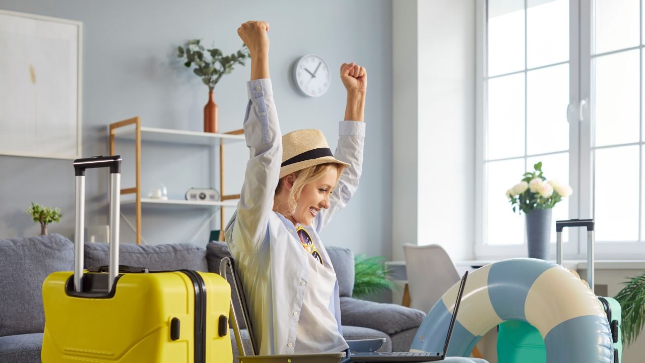 Joyful woman tourist happy to reserve travel ticket, going to spend summer vacations abroad, packed things in suitcase, focused at laptop screen and clenching fists with success. Tourism concept