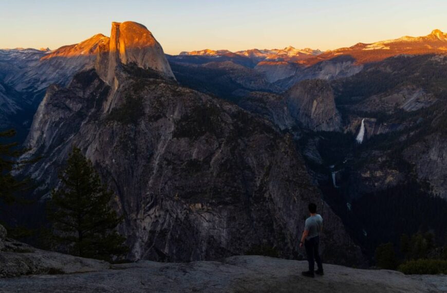 a hiker looks out at half dome at sunset from glacier point