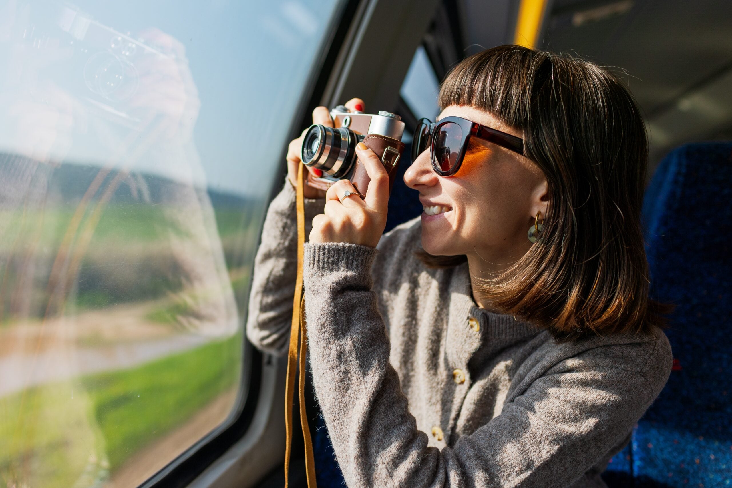 A beautiful, happy young woman takes a photo with a vintage analog camera from a train window. Concept of travel and discovery. A female tourist traveling by train.