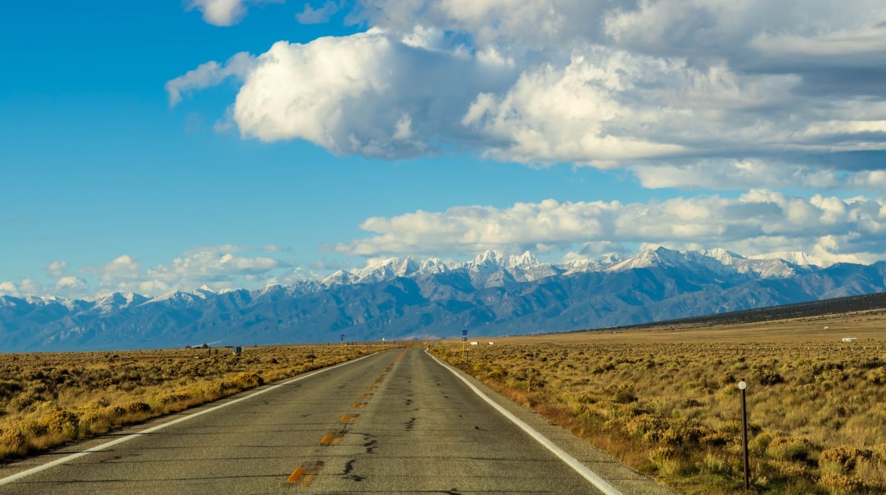 a paved highway leading towards mountains with clouds in the sky