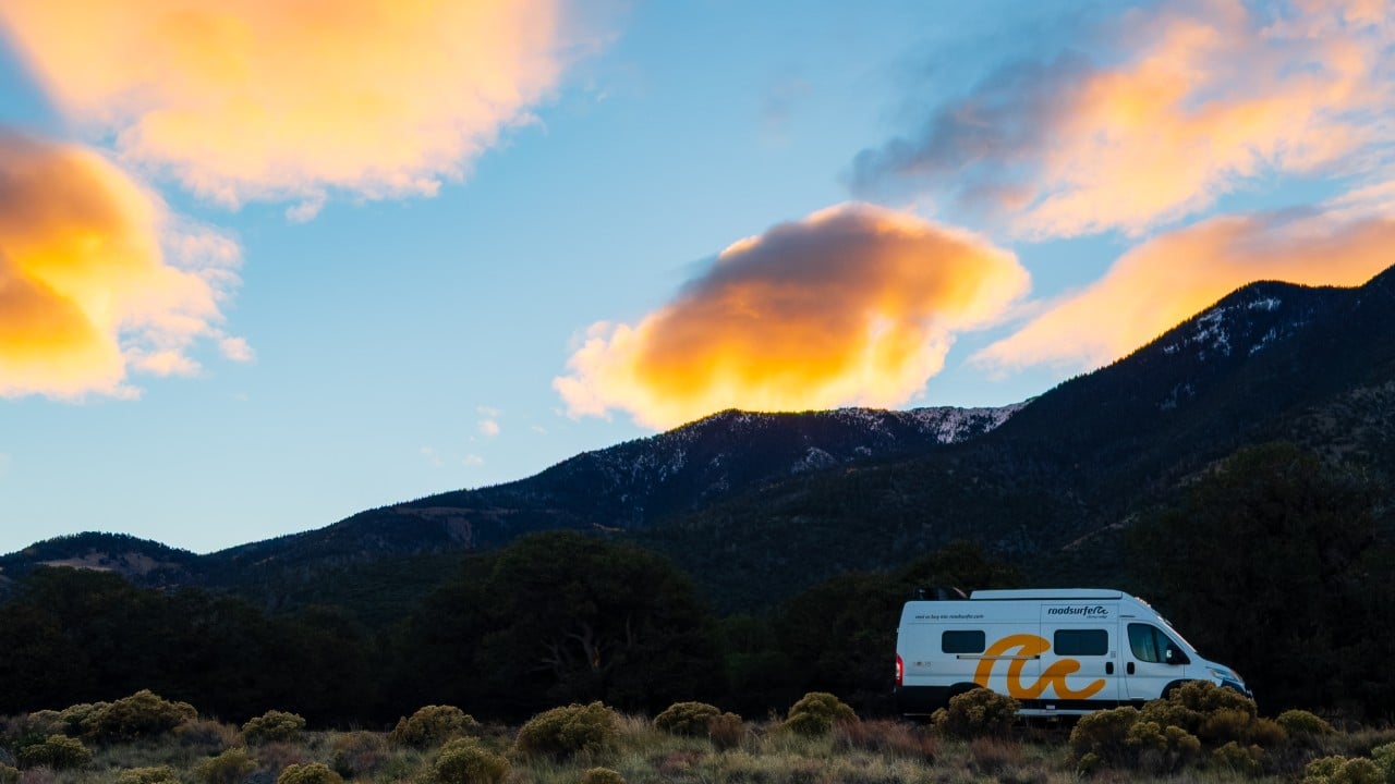 a roadsurfer camper van parked along the road with sunrise colors in the clouds above it