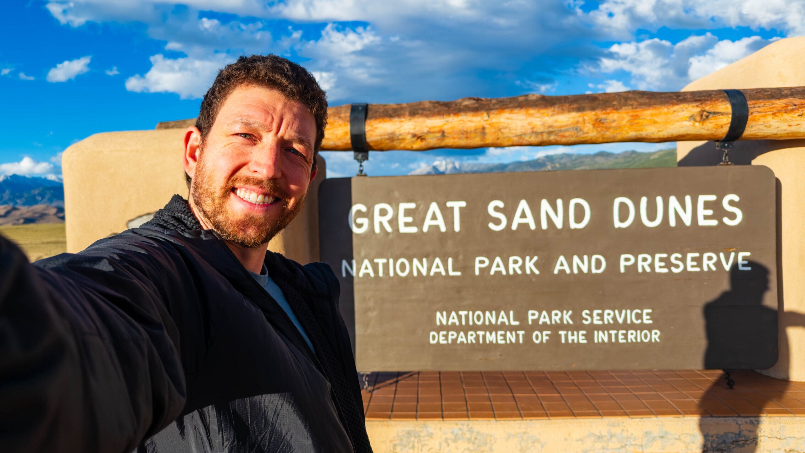 a visitor selfies in front of the great sand dunes national park sign